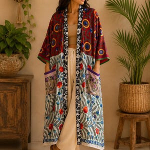 May include: A long, open-front kimono featuring a vibrant, multi-coloured floral embroidery pattern. The upper section is deep red, while the lower portion is white. It includes a black and white floral trim, wide sleeves, and two purple-lined pockets.