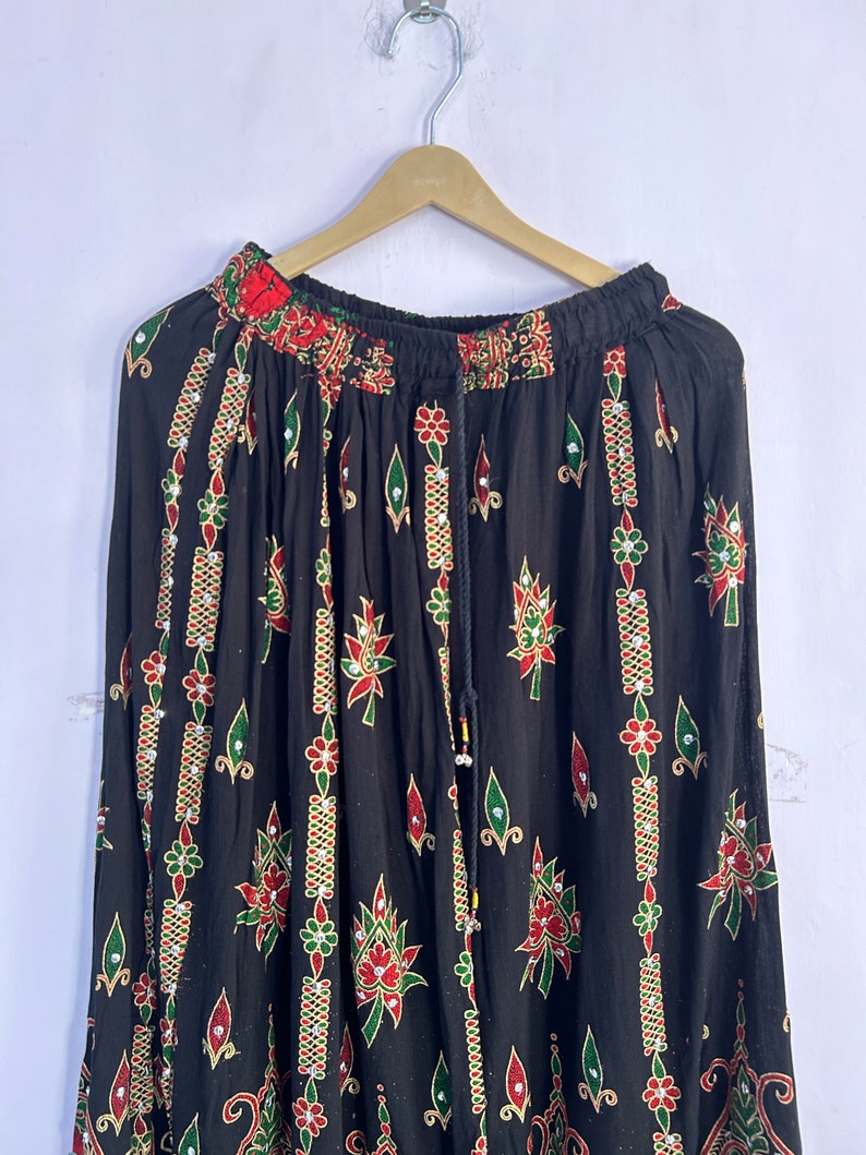 May include: A black skirt with a floral print and beaded embellishments. The skirt has an elastic waistband and a drawstring closure.