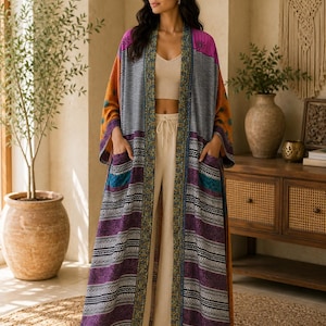 May include: A long, open-front kimono-style robe featuring a vibrant mix of purple, orange, and black patterns. The garment includes wide sleeves, two large front pockets, and a decorative border trim with intricate floral and geometric designs.