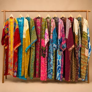 Puede incluir: Una colección de diez batas de manga larga colgadas en un perchero de madera. Cada bata presenta un diseño de patchwork único con colores vibrantes que incluyen rojo, amarillo, azul, rosa y verde, mostrando varios patrones florales y geométricos.