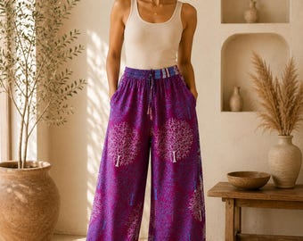 May include: A beige ribbed tank top paired with wide-leg trousers in a vibrant purple hue. The trousers feature a repeating white tree pattern, a drawstring elastic waistband, and a blue and white chevron-patterned border at the hemline.