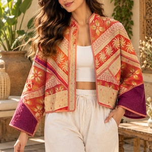 May include: A cropped open-front jacket featuring a quilted texture with a vibrant pattern of orange, red, and cream floral motifs. The garment includes wide sleeves with solid purple cuffs and a mandarin-style collar, worn over a white top and pants.