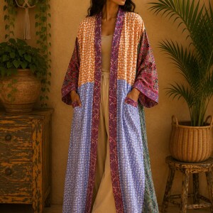 May include: A long, open-front kimono robe featuring a patchwork design with panels of orange, light blue, and green fabric, all adorned with a repeating leaf pattern. The garment includes a dark purple trim and two front patch pockets.