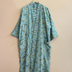 May include: A light blue paisley print robe with long sleeves and pockets. The robe is hanging on a wooden hanger. The paisley pattern includes yellow and green accents.