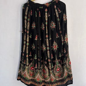 May include: A black maxi skirt with a floral print and gold and red accents. The skirt has a wide elastic waistband and a flowing silhouette.