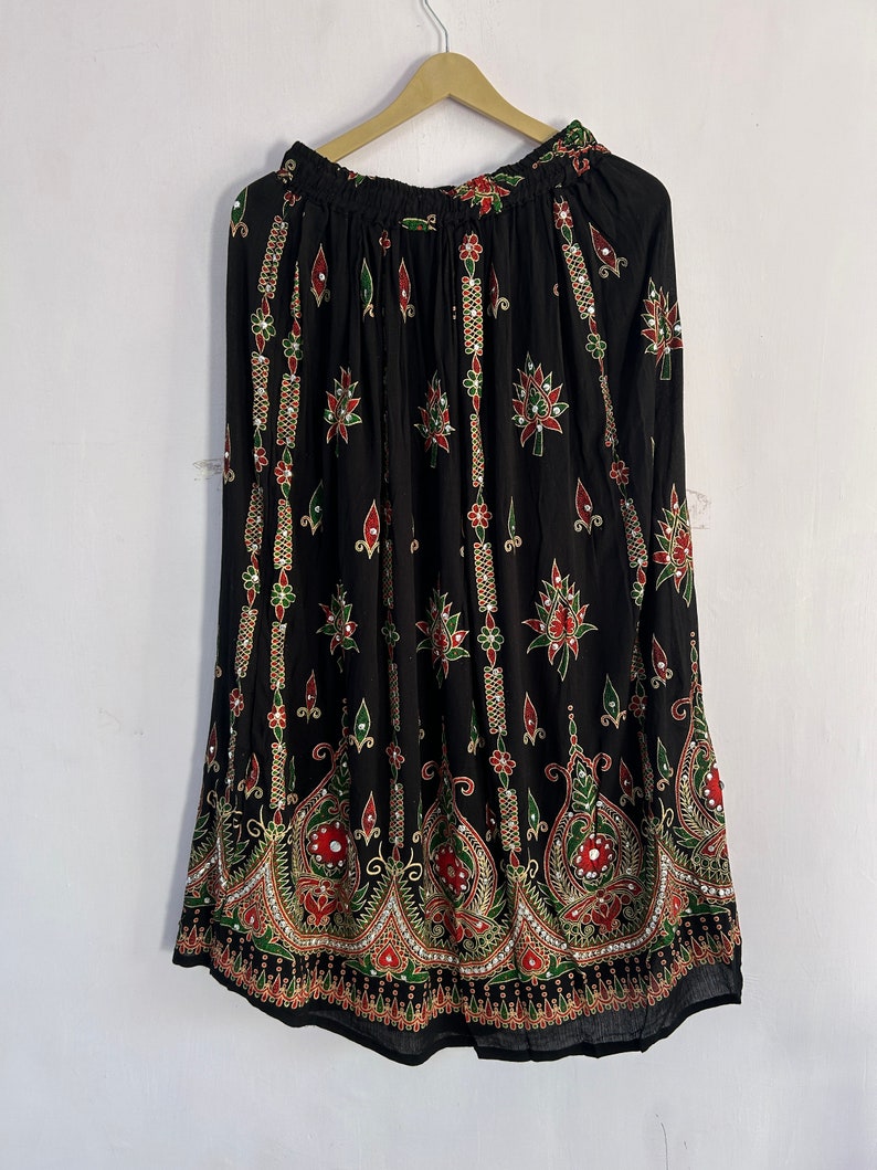 May include: A black maxi skirt with a floral print and gold and red accents. The skirt has a wide elastic waistband and a flowing silhouette.