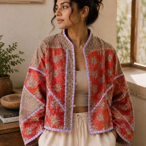 May include: A quilted jacket featuring a vibrant red base with a repeating floral pattern in muted green and tan. The garment has a mandarin collar, wide sleeves, and contrasting trim in a blue and white geometric print along the front edges.