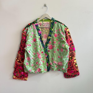 May include: A long-sleeve jacket featuring a light green base with pink floral embroidery and green leaf patterns. The sleeves are a contrasting red with intricate floral and paisley embroidery. The garment has a V-neckline and a dark green trim.