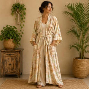 May include: A long, open-front robe featuring a light beige and cream floral pattern with wide sleeves and two front patch pockets. The robe is worn over a matching light beige sleeveless jumpsuit with wide-leg trousers, creating a coordinated set.