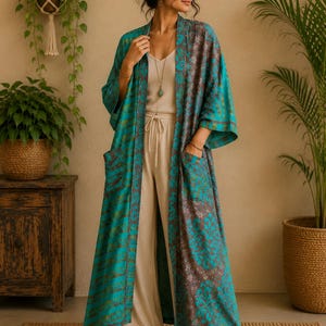 Puede incluir: Un kimono largo abierto por delante con un vibrante estampado de damasco en color verde azulado y marrón. La prenda tiene mangas anchas de tres cuartos, dos grandes bolsillos delanteros y un dobladillo recto que llega a la pantorrilla.