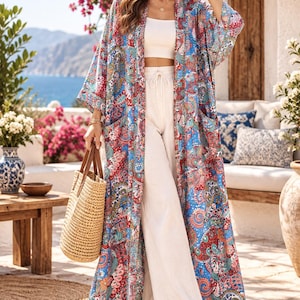 Może przedstawiać: Długie kimono z otwartym przodem, ozdobione wyrazistym, wielokolorowym wzorem paisley w odcieniach niebieskiego, czerwonego i pomarańczowego. Ubiór posiada szerokie rękawy o długości trzy czwarte, dwie naszywane kieszenie i luźny, długi krój.