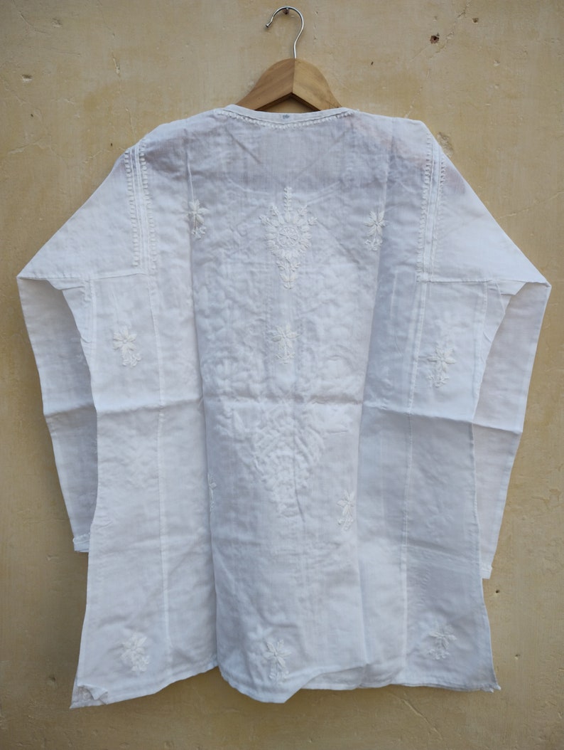 May include: White cotton tunic with white embroidery. The embroidery features a floral design.