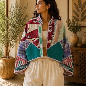 Puede incluir: Una chaqueta corta abierta por delante con un diseño de patchwork que presenta varios patrones geométricos y florales en tonos rojo, verde azulado, morado y blanco. La prenda tiene mangas anchas de tres cuartos y un cuello mao con costuras visibles.