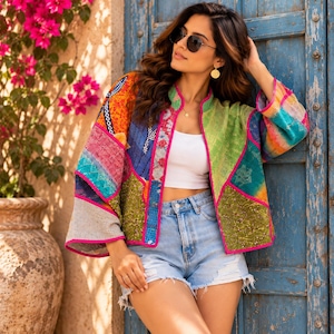 Peut inclure: Une veste à manches longues ouverte sur le devant, présentant un motif patchwork vibrant avec diverses sections colorées en vert, orange, bleu et rose. La veste est dotée d'un liseré rose vif sur les bords et se porte sur un haut court blanc.
