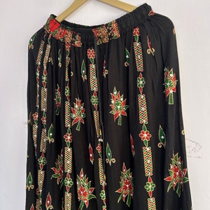 May include: Black maxi skirt with a floral print and gold accents. The skirt has an elastic waistband and a drawstring closure.
