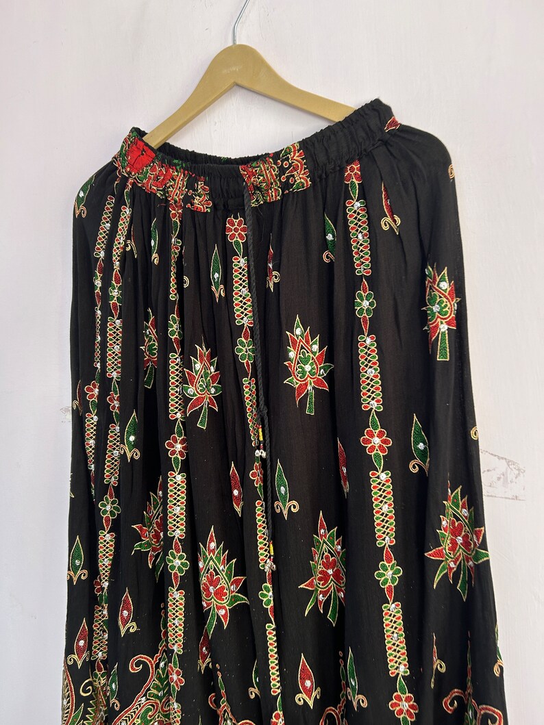 May include: Black maxi skirt with a floral print and gold accents. The skirt has an elastic waistband and a drawstring closure.