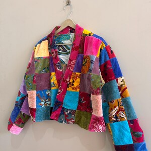 May include: A patchwork jacket in a variety of colors, including pink, blue, purple, and yellow. The jacket is made of different fabrics and patterns, creating a unique and vibrant design. The jacket is hanging on a wooden hanger.