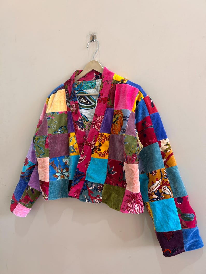 May include: A patchwork jacket in a variety of colors, including pink, blue, purple, and yellow. The jacket is made of different fabrics and patterns, creating a unique and vibrant design. The jacket is hanging on a wooden hanger.