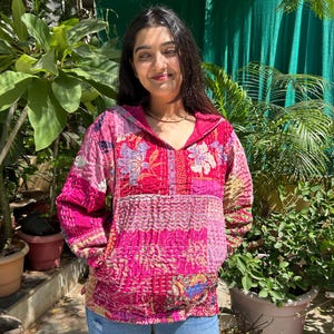 May include: A pink quilted jacket with floral embroidery and a hood. The jacket is made of patchwork fabric and has a relaxed fit.