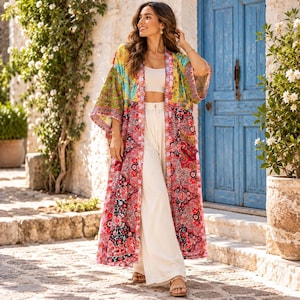 Puede incluir: Un kimono largo abierto por delante con un vibrante estampado de retazos florales y de cachemira en tonos amarillo, verde, rosa, rojo y negro. La prenda se lleva sobre un top corto blanco liso y pantalones anchos a juego con sandalias.