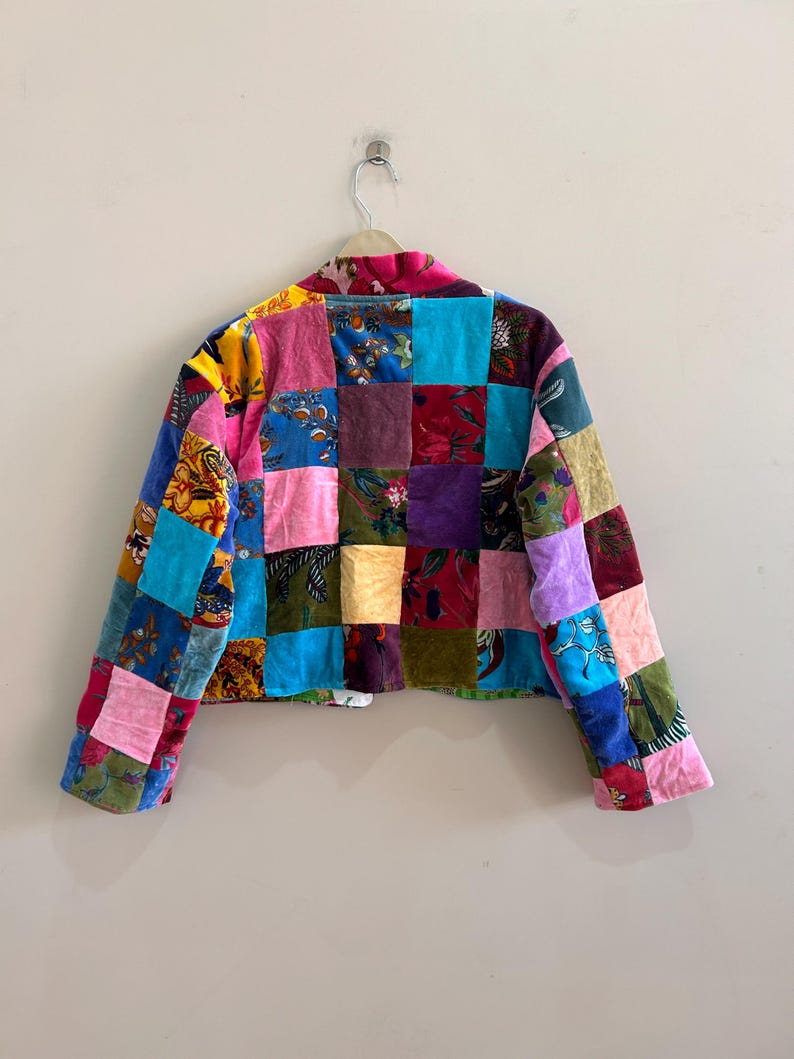 May include: A patchwork jacket with a vibrant mix of colors and patterns. The jacket features a variety of fabrics in squares of pink, blue, green, purple, and yellow. The jacket is hanging on a white hanger.