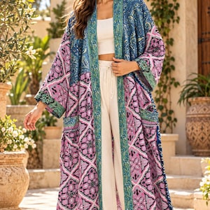 May include: A long, open-front kimono featuring a vibrant patchwork design with shades of blue, pink, and black. The garment includes a prominent teal paisley border along the front opening and wide sleeves, paired with a white crop top and trousers.