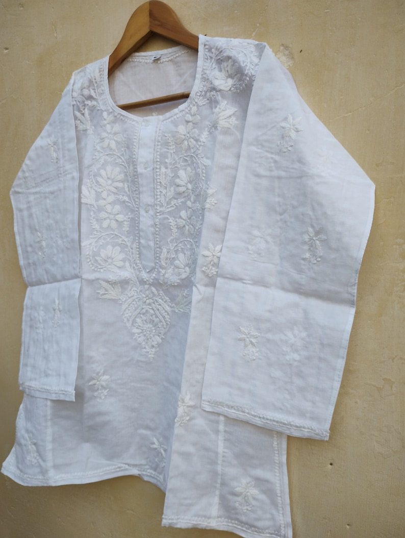 May include: White cotton tunic top with delicate white embroidery. The top has a round neckline and long sleeves.