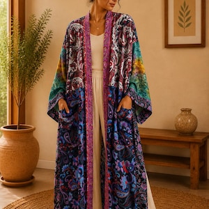 May include: A long, open-front kimono robe featuring a vibrant, multi-coloured paisley and floral pattern in shades of deep blue, purple, teal, and magenta. The garment includes wide sleeves, a contrasting patterned trim along the front, and two pockets.