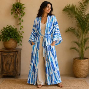 May include: A long, open-front robe featuring a blue and white tie-dye pattern, wide sleeves, and a matching tie belt at the waist. The garment includes two large patch pockets on the front and falls to the ankles, worn over a beige tank top and trousers.