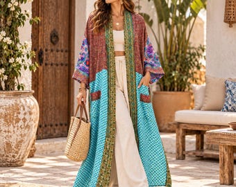 May include: A long, open-front kimono featuring a vibrant patchwork design with shades of turquoise, deep red, and intricate floral patterns. The garment includes a decorative green border, two front pockets, and wide sleeves, worn over a white top and pants.