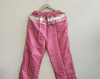 Puede incluir: Pantalones rosas con un patrón floral blanco repetitivo, cintura elástica con cordón y una banda horizontal ancha con un diseño geométrico azul y blanco en los dobladillos superior e inferior, colgados en una percha gris.