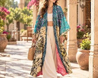 Può includere: Un lungo kimono aperto sul davanti caratterizzato da un patchwork di motivi floreali e astratti nei toni del verde acqua, crema, verde oliva e rosa. Il capo è indossato sopra un top corto bianco e pantaloni ampi, abbinato a una borsa in paglia intrecciata.