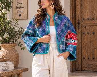May include: A cropped, open-front jacket featuring a patchwork design of blue, purple, and teal plaid patterns with a contrasting red and white patterned panel on the left sleeve, finished with bright teal trim along the edges and wide sleeves.