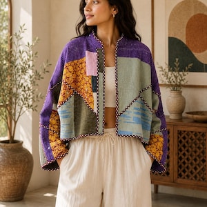 Peut inclure: Une veste courte ouverte sur le devant, confectionnée en tissu patchwork matelassé avec un mélange de motifs floraux violets, vert sauge et jaune moutarde. Le vêtement présente des manches longues, un col officier et un liseré foncé.