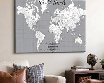 May include: A rectangular wall canvas featuring a world map in white against a grey grid background. The text World Travels is printed in black script at the top, and the text The Johnson Family is printed in black at the bottom centre.