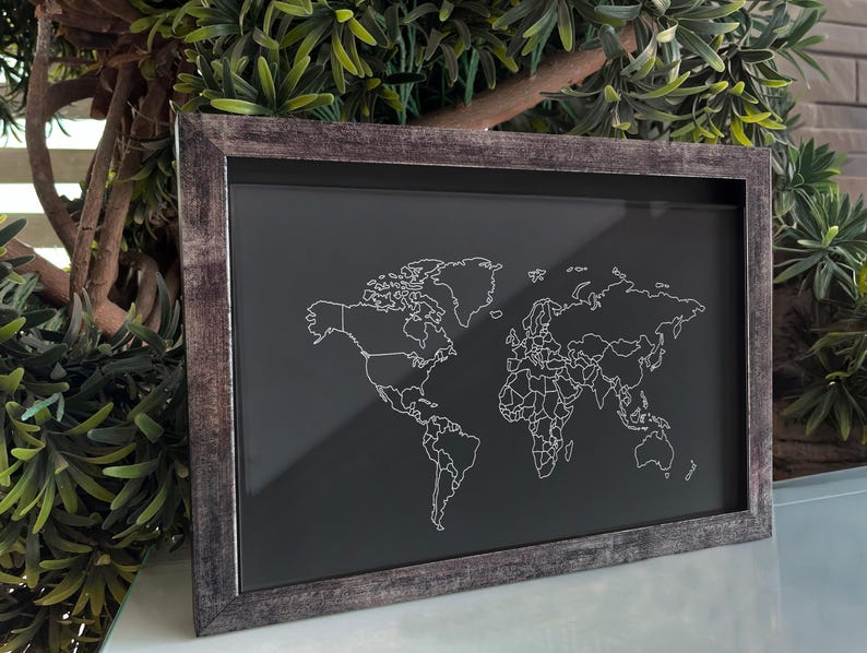 May include: A rectangular wall art piece featuring a world map with white outlines on a solid black background. The map is enclosed in a weathered, dark gray wooden frame with a textured finish, displaying continental borders and landmass shapes.