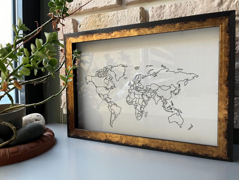 May include: A black frame with a gold trim surrounds a white map of the world. The map shows the continents and countries in black lines.