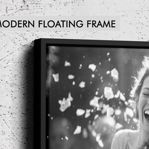 May include: A black floating frame containing a black and white photograph of a laughing person with falling petals. The text MODERN FLOATING FRAME is printed in black on a light gray background above the frame, which has a thin black border.