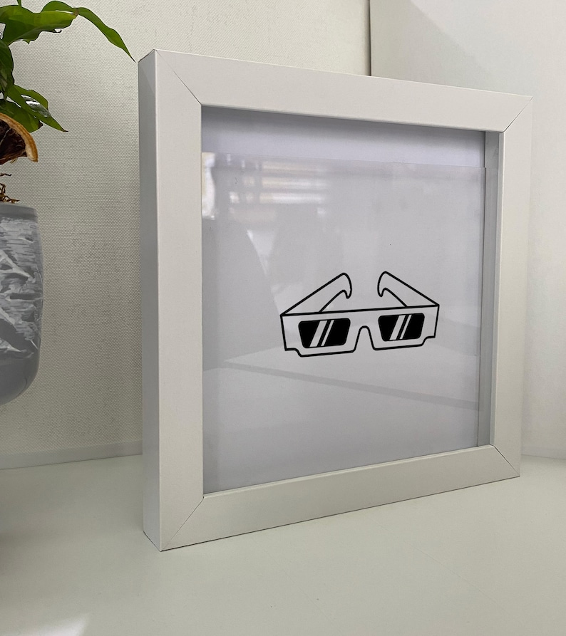 May include: A white picture frame with a clear acrylic front. The frame contains a black and white line drawing of a pair of 3D glasses.