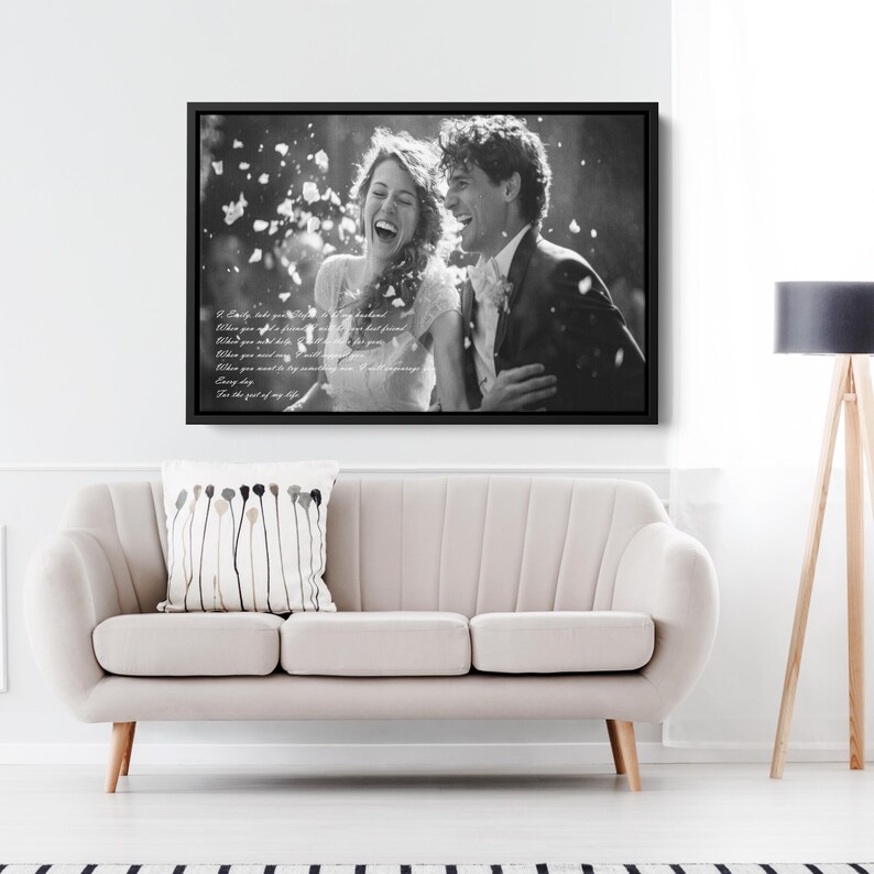 May include: A black and white framed wall art print featuring a laughing couple in wedding attire surrounded by falling petals. The image includes overlaid white text of wedding vows, all encased in a thin black frame hanging on a wall.