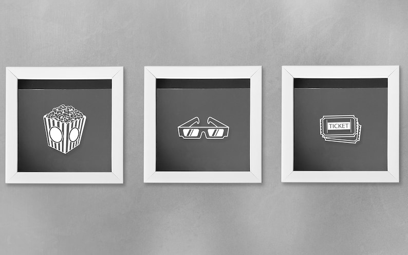 May include: Three white picture frames with black mats, each featuring a different movie-themed icon: a bucket of popcorn, 3D glasses, and a movie ticket.