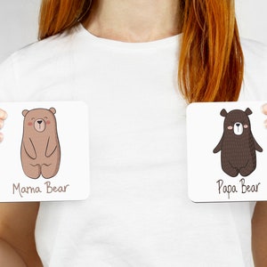 May include: Two square coasters, each featuring a cartoon bear illustration. One coaster reads "Mama Bear" and depicts a light brown bear. The other reads "Papa Bear" and shows a dark brown bear.