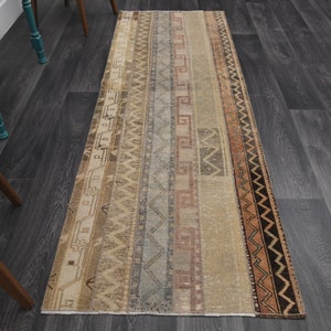 May include: A vintage runner rug with a beige background and colorful geometric patterns. The rug has a faded look and is made of woven fabric.