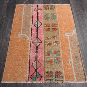 Può includere: Un tappeto vintage con un motivo geometrico in tonalità arancio, rosa e blu. Il tappeto ha un aspetto sbiadito e usurato, che gli conferisce un fascino unico e rustico.