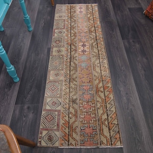May include: A long, narrow rug with a beige background and intricate patterns in shades of orange, brown, and blue. The rug has a distressed, vintage look.