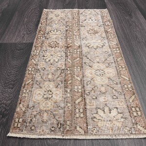 May include: A vintage style runner rug with a beige and brown floral pattern. The rug has a frayed edge and is made of a soft, woven material.