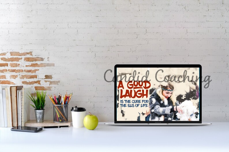 May include: A laptop computer screen displaying a motivational quote: "A good laugh is the cure for the ills of life." The quote is in red and white lettering on a background of a woman laughing in the snow. The laptop is on a white desk with a white coffee cup, a green apple, a pencil holder, a plant, and a stack of books.