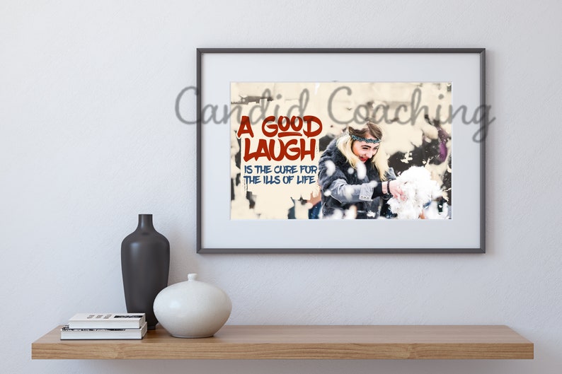 May include: A framed print with a woman laughing and throwing snow in the air. The print has the text "A good laugh is the cure for the ills of life" in red and blue letters.