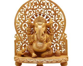 Op de afbeelding: Gedetailleerde houten snijwerk van de hindoe-godheid Ganesha, zittend op een decoratief platform. De sculptuur heeft ingewikkelde bloemen- en geometrische patronen, met een muis aan de basis. Het snijwerk is in een natuurlijke houttint.