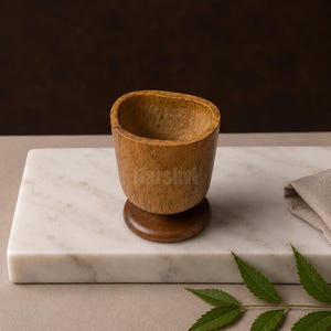 Könnte beinhalten: Ein kleiner, hellbrauner Holzbecher mit einer abgerundeten Schale und einem runden Fuß. Der Becher weist eine sichtbare Holzmaserung auf der gesamten Oberfläche auf, mit einem leicht unregelmäßigen, organischen Rand und einem glatten Fuß.